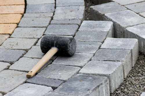 A black rubber mallet with a wooden handle is resting on gray stone pavers arranged in a pattern on the ground.